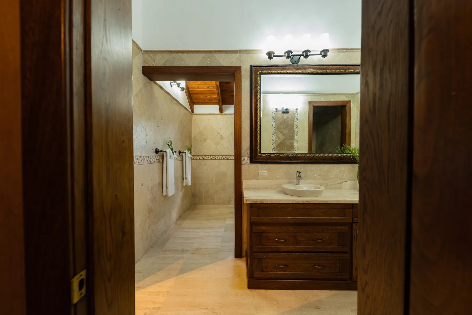 A bathroom with a sink and mirror, viewed through an open doorway.