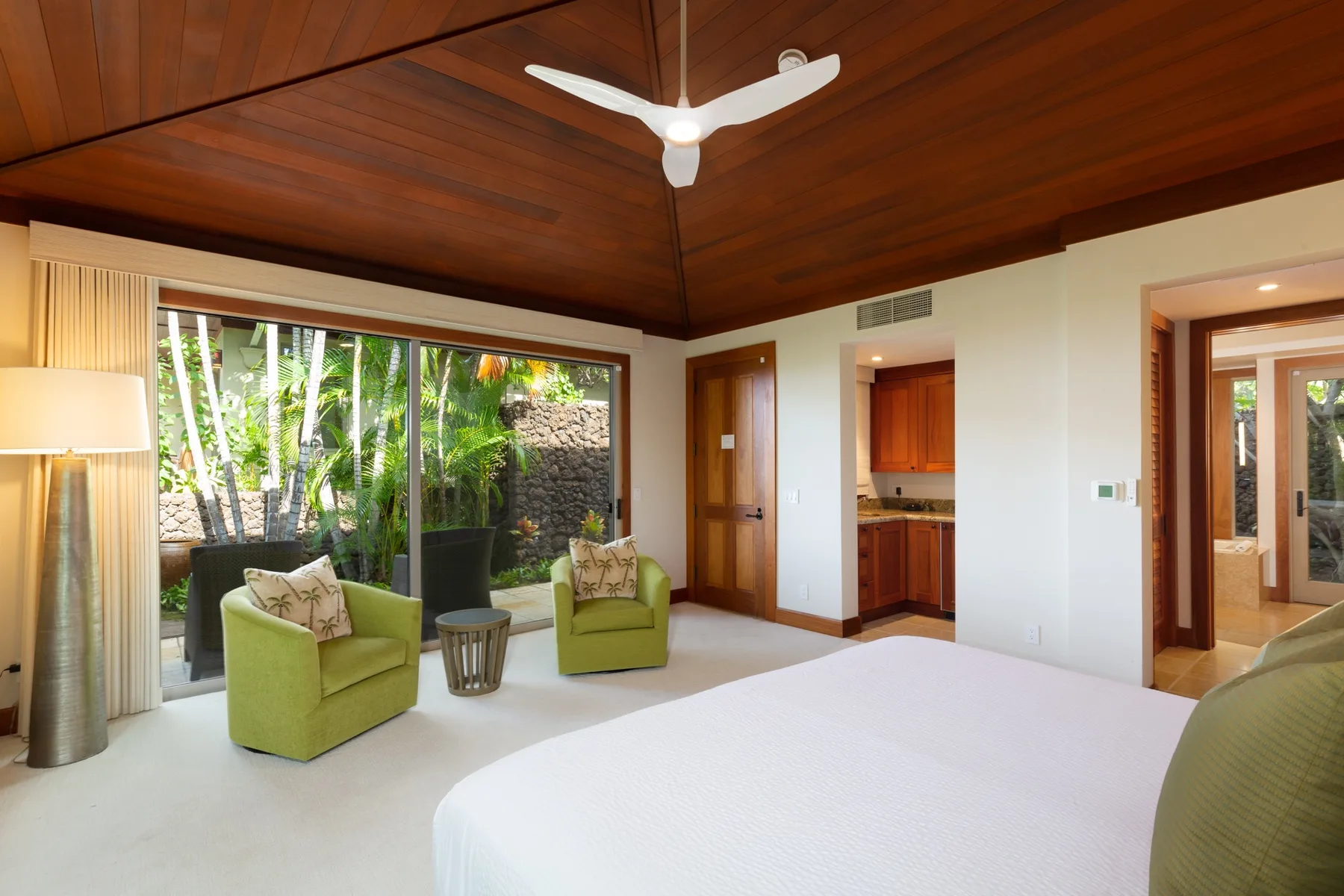 A bright bedroom with a large bed, seating, and sliding glass doors opening onto a garden.
