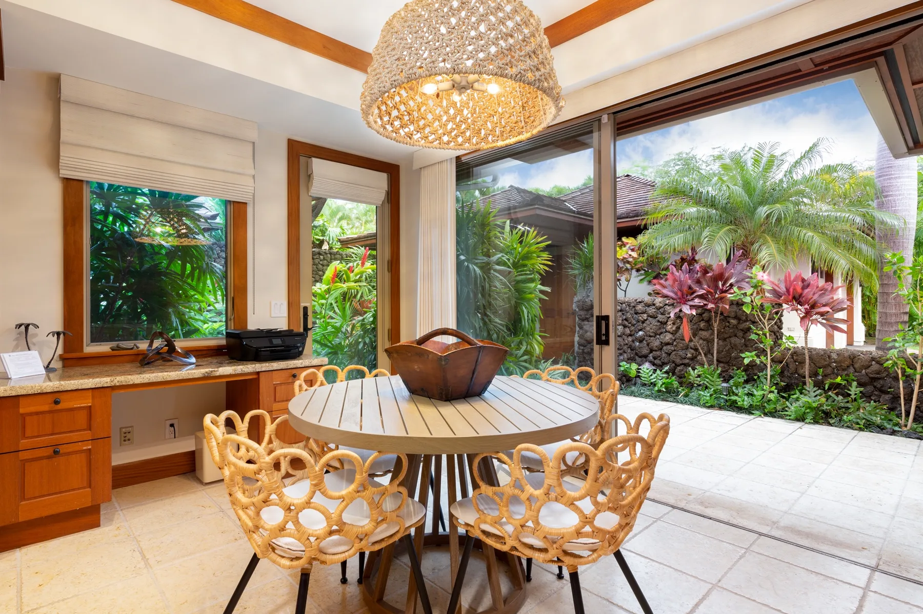 A dining area with a round table beside large windows overlooking a tropical garden.
