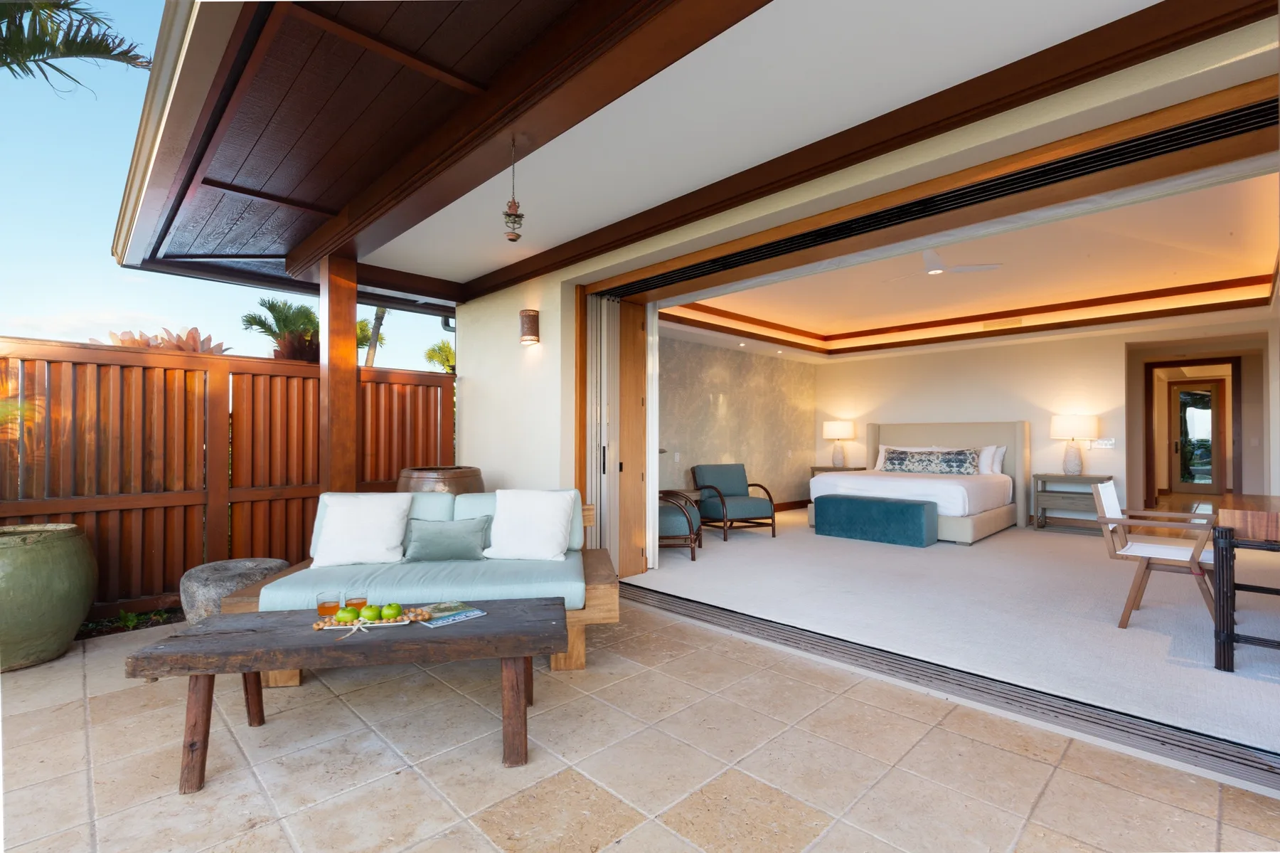 A bedroom opens onto a covered patio with seating and a wooden privacy screen.