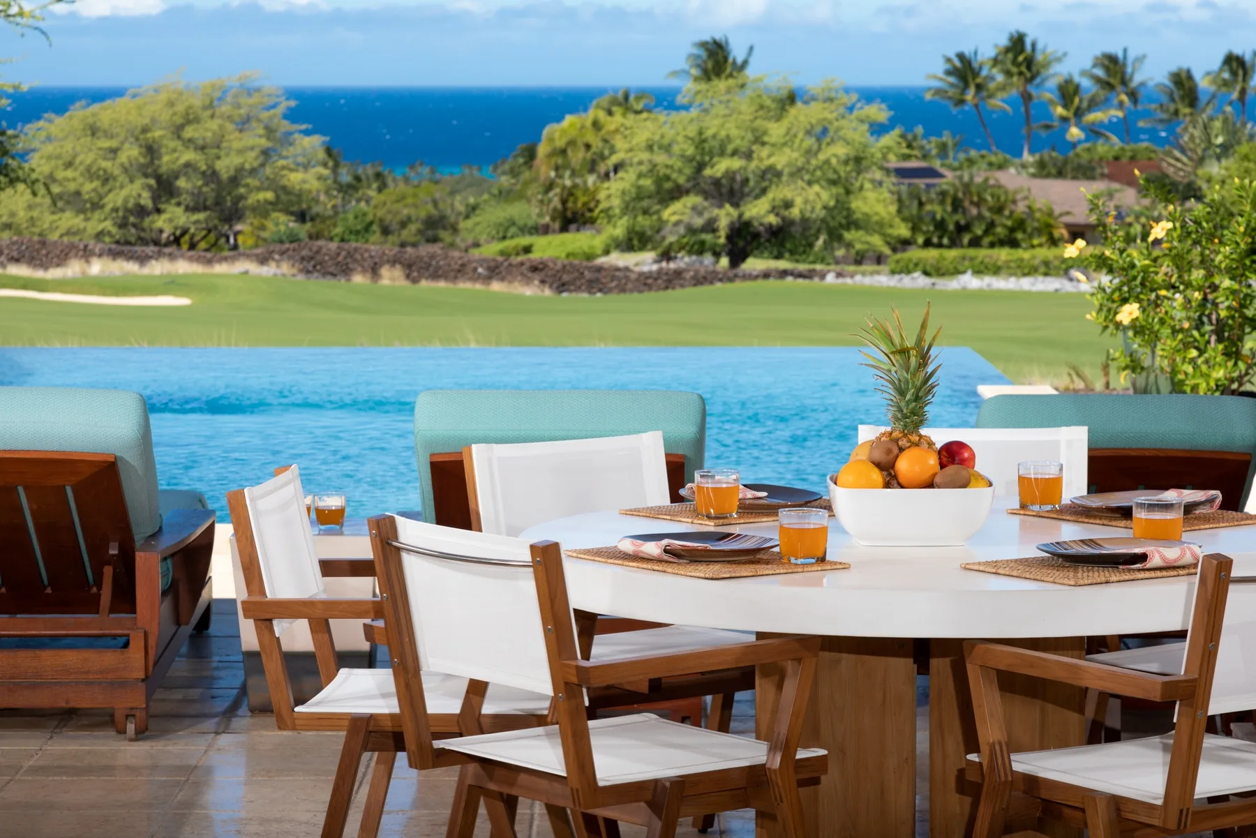 An outdoor dining table with chairs overlooks a swimming pool and ocean.