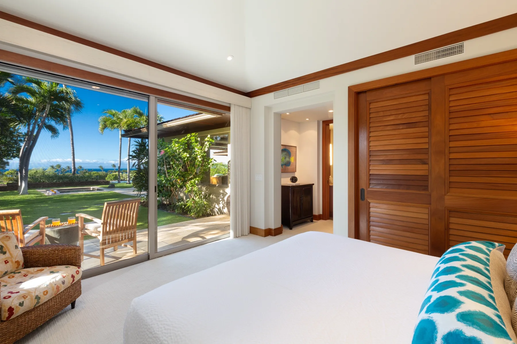 A bright bedroom with a large bed, sliding glass doors, and a tropical garden view.