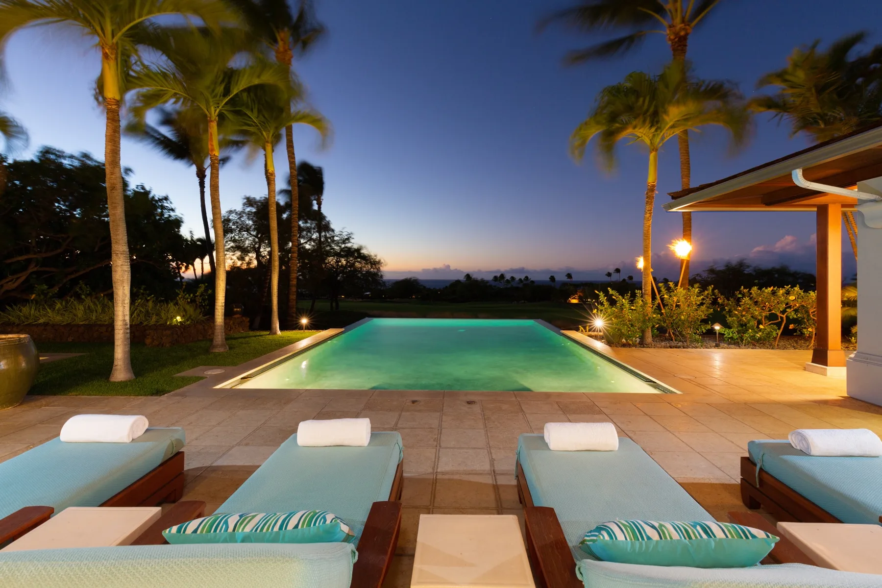 An outdoor pool at dusk, with palm trees and lounge seating.