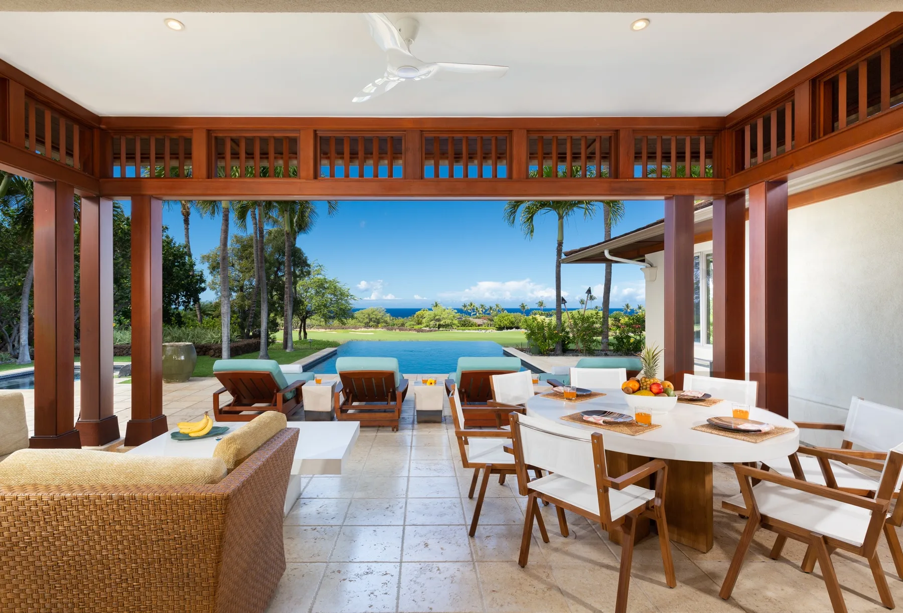 An open-air dining area with a long table and a pool visible beyond it.