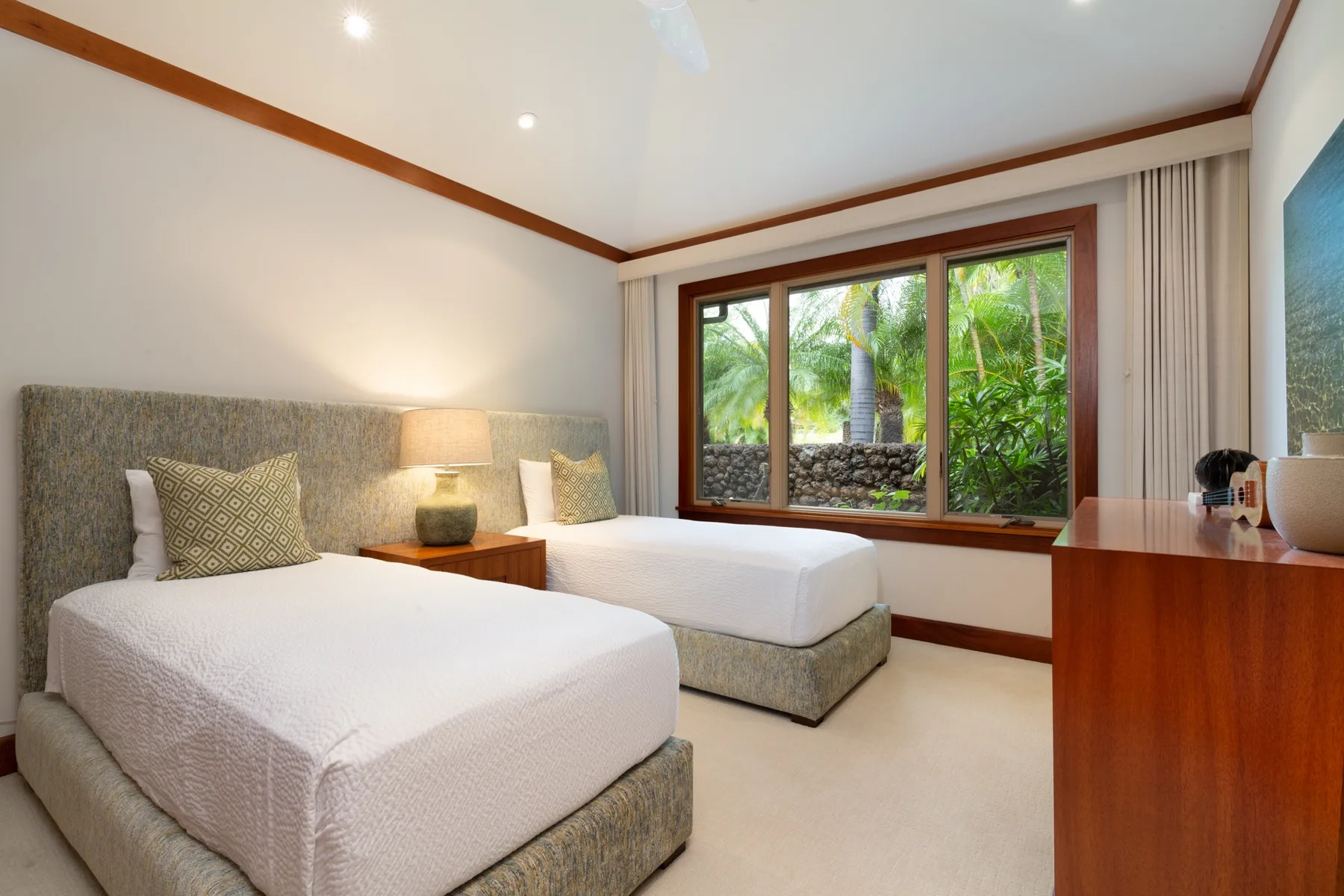 A bright bedroom with two beds and a large window overlooking greenery.