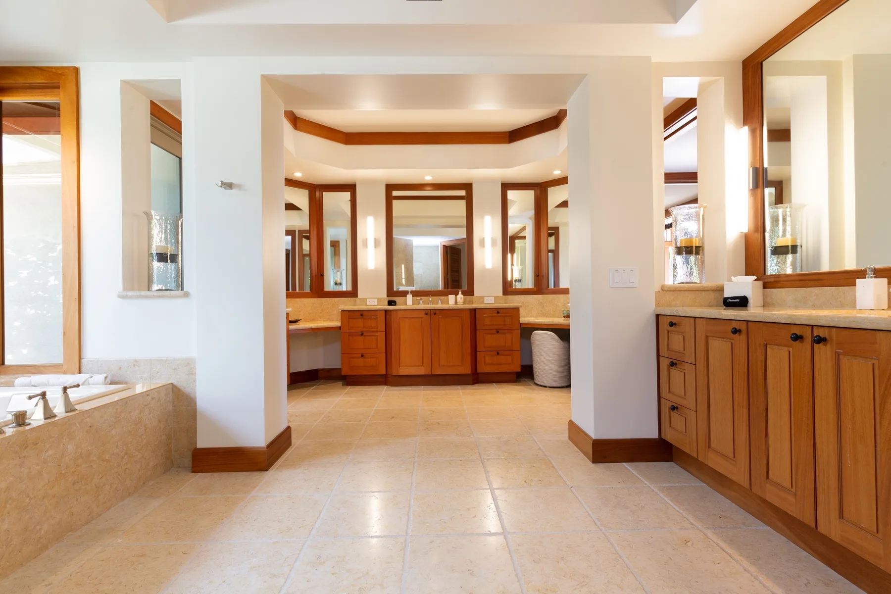 A spacious bathroom with wood cabinetry, large mirrors, and a tiled floor.
