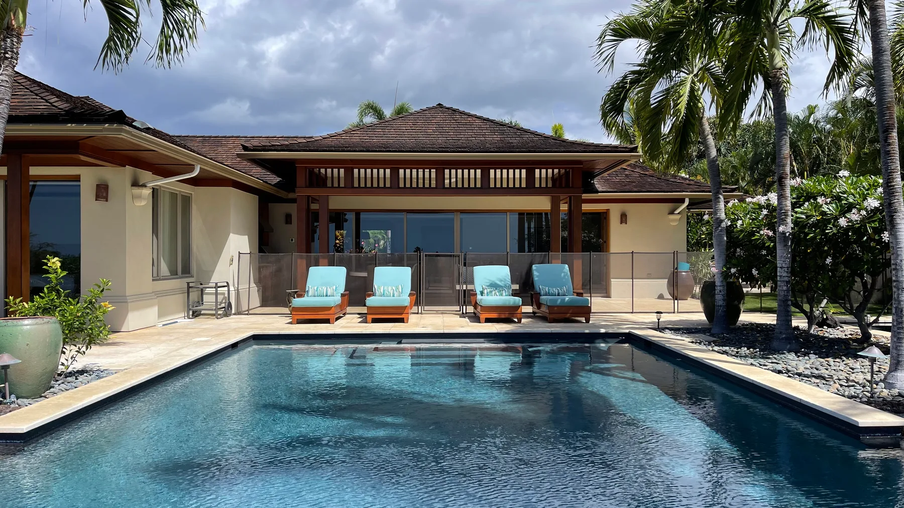A swimming pool in front of a house, with palm trees around it.