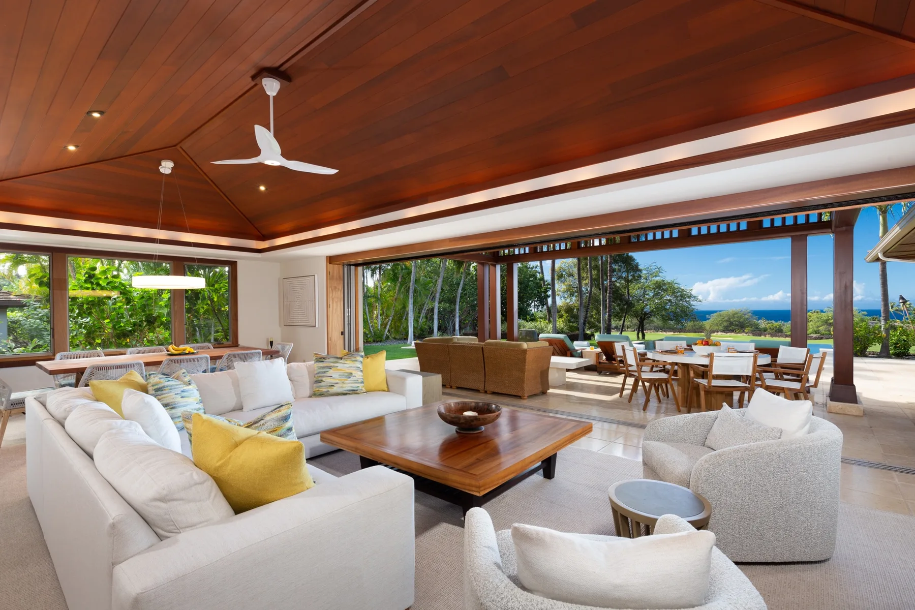 An open living area has white seating and broad windows overlooking greenery and the water.