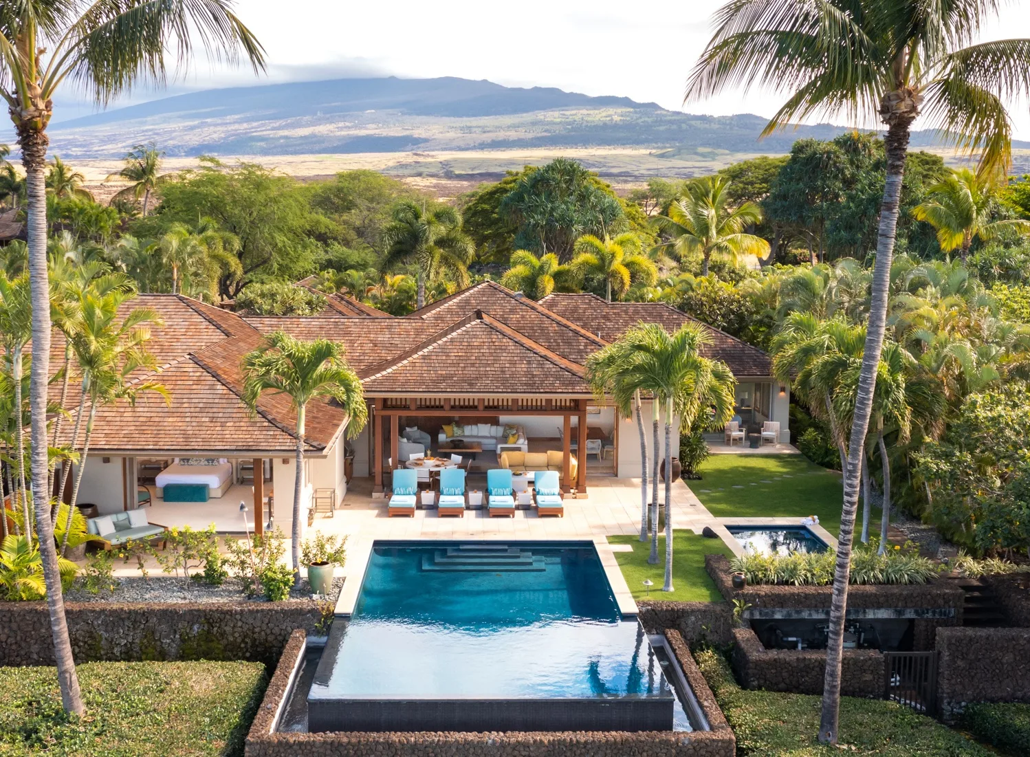 A tropical villa with a pool and palm trees, surrounded by lush greenery.