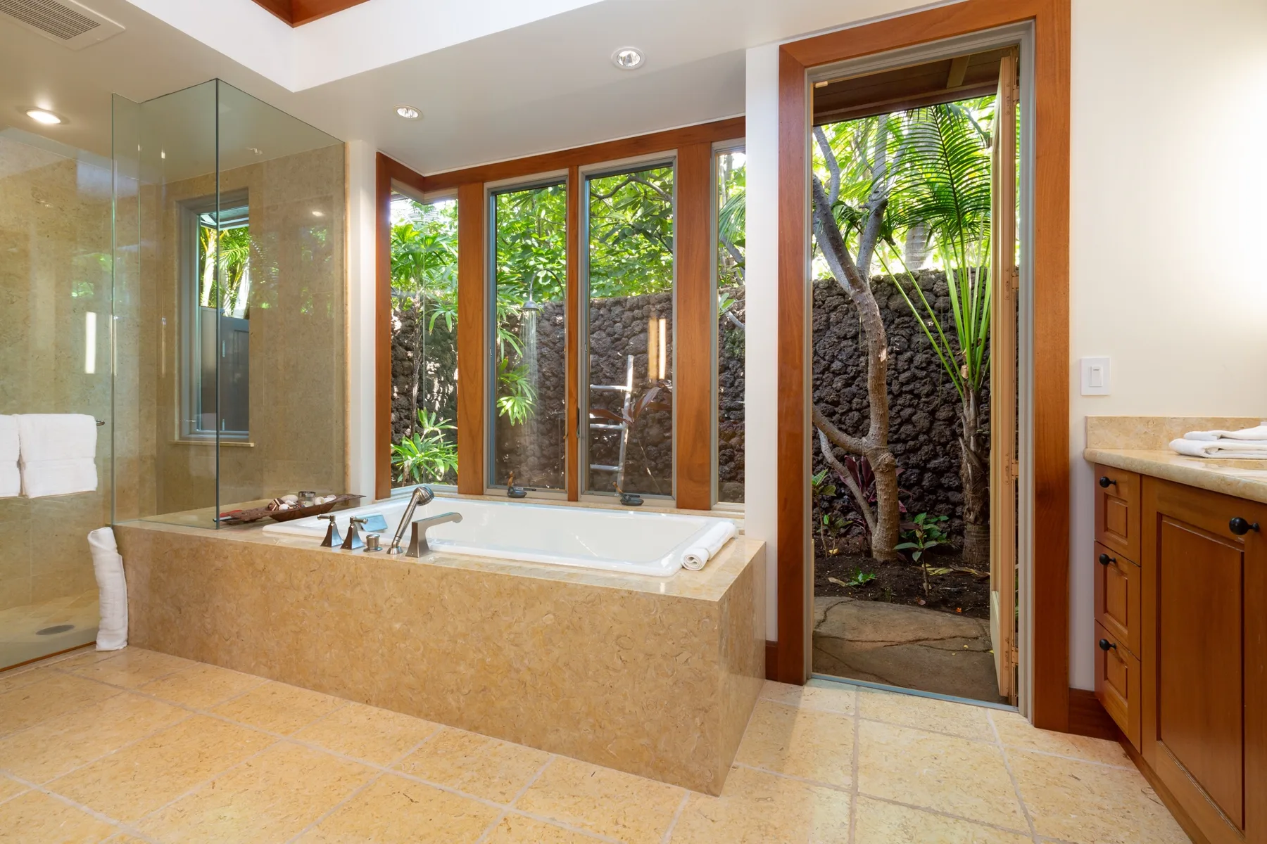 A bright bathroom with a bathtub beside large windows overlooking greenery.
