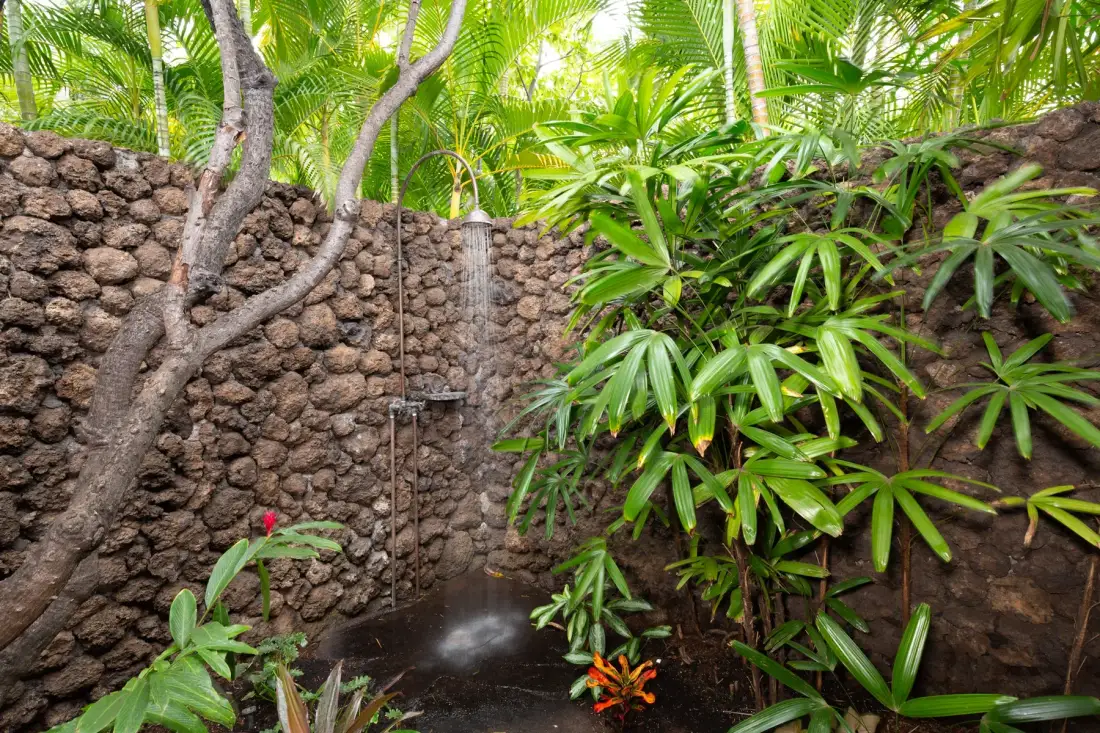 A garden shower sits among tropical plants and stone walls.