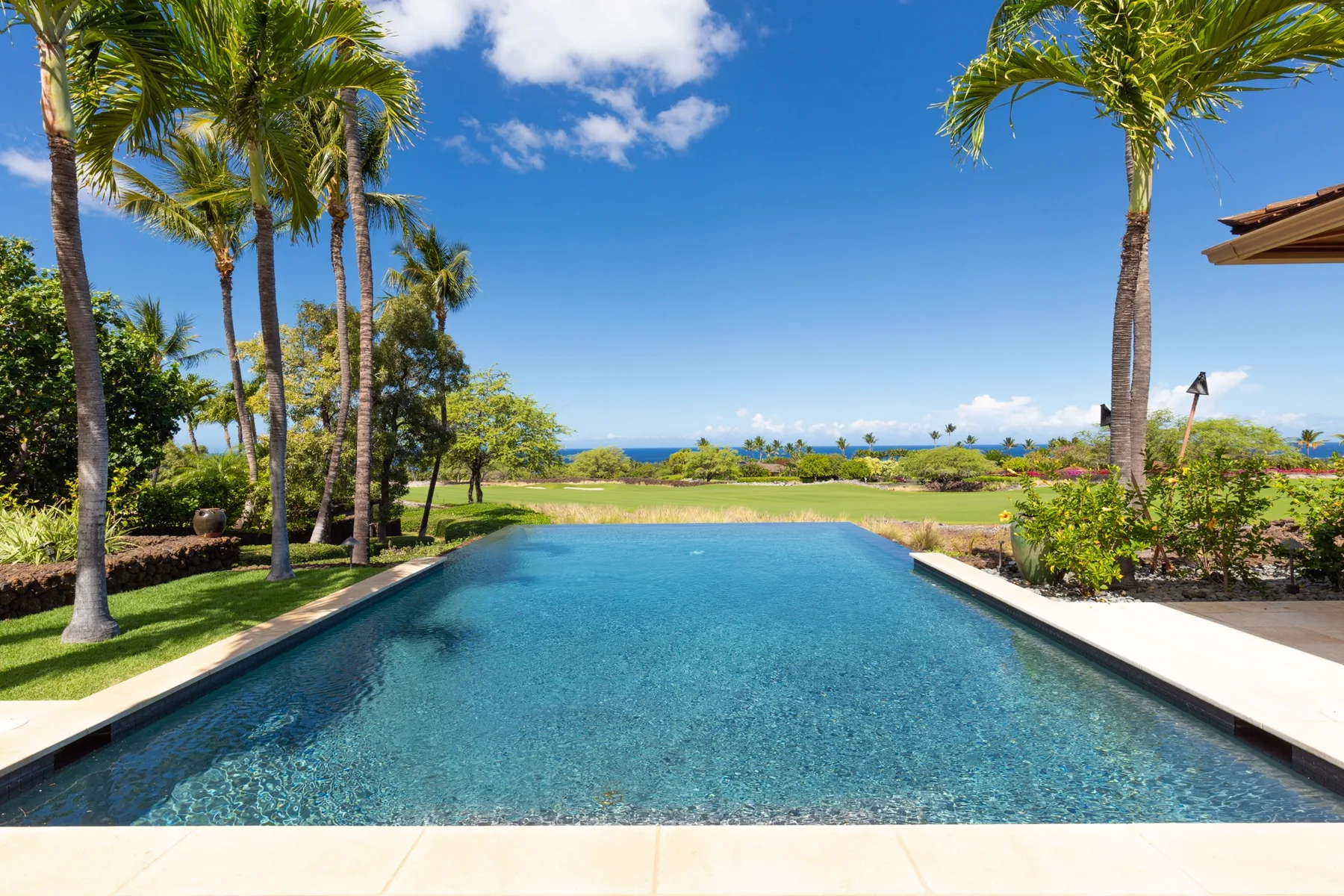 A swimming pool overlooks landscaped grounds and the ocean beneath a sunny sky.
