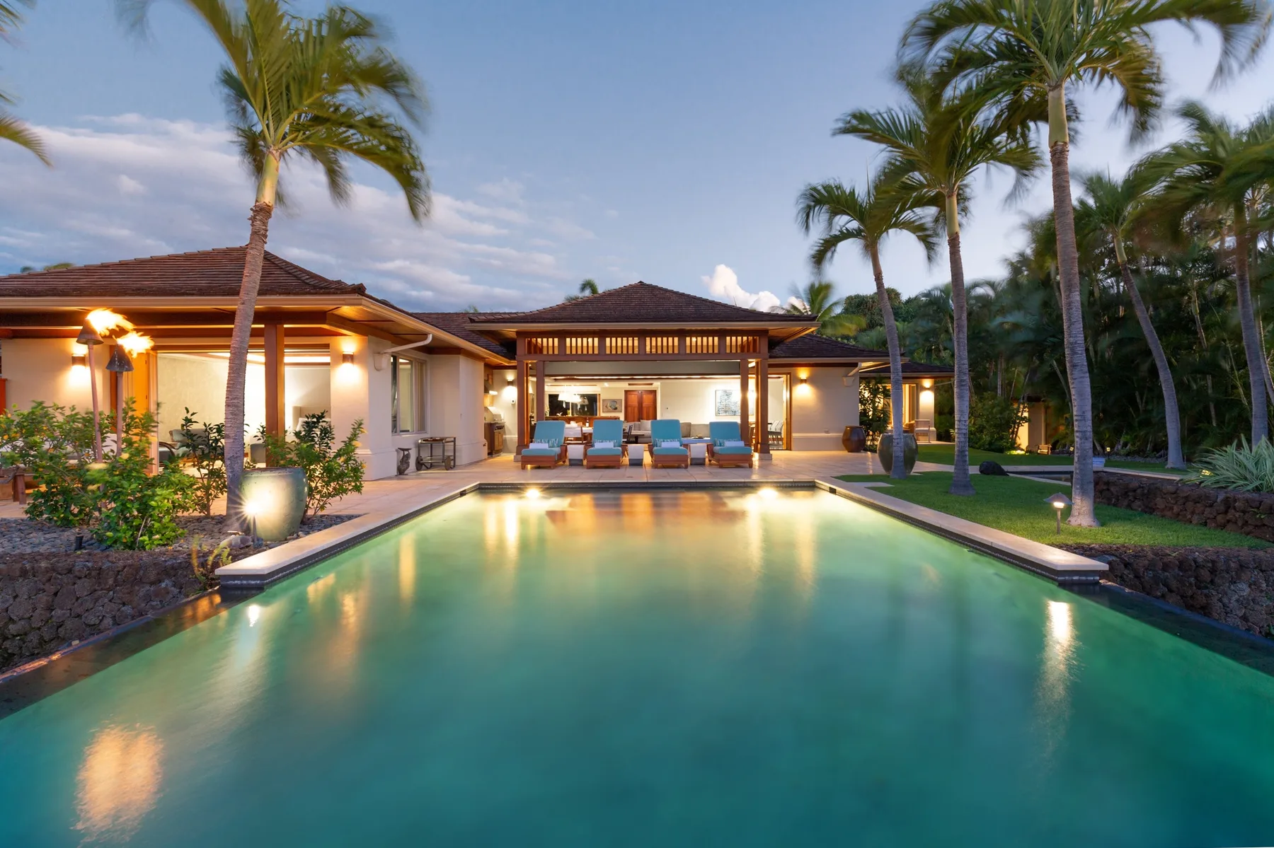 A swimming pool in front of a warmly lit building with palm trees.