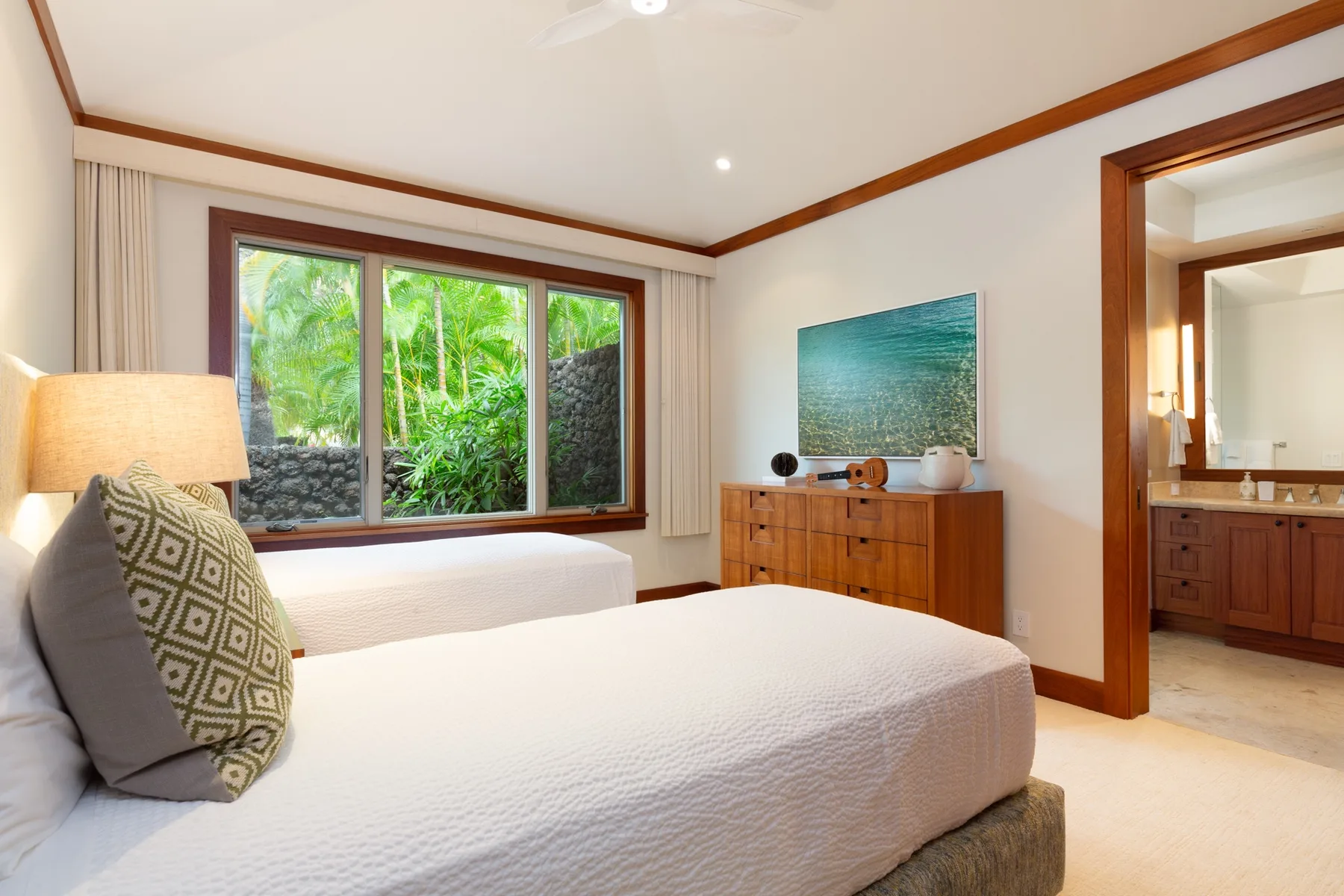 A bedroom with two beds, a dresser, and a window overlooking greenery.