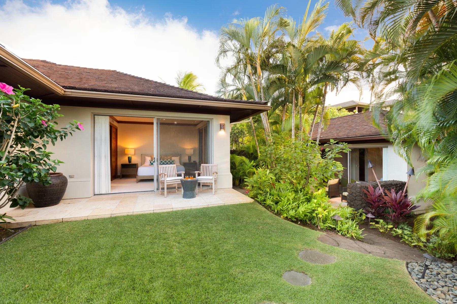 A garden lawn leads to a patio and a room with sliding glass doors.
