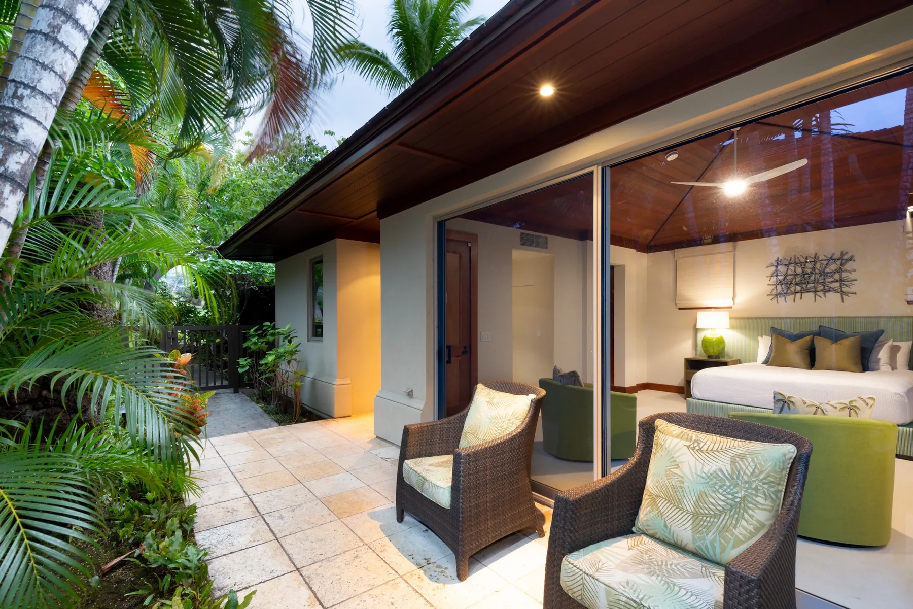 A bedroom opens onto a tiled patio with cushioned seating and tropical plants.