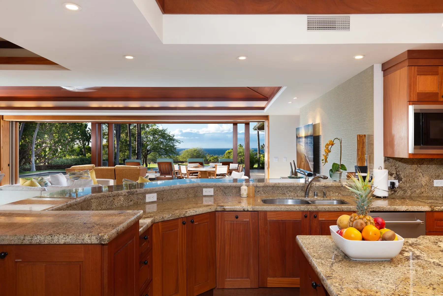 A spacious kitchen with a stone island and large windows overlooking greenery.