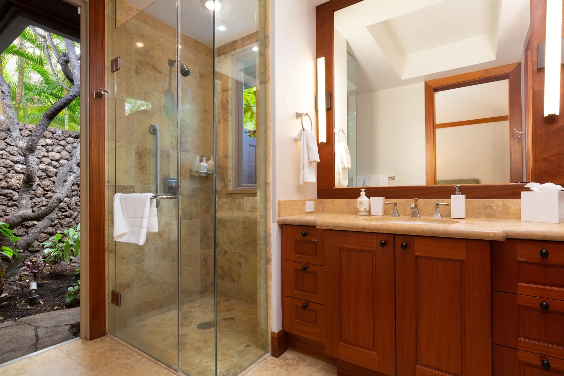 A bathroom with a glass shower and a wooden vanity beneath a large mirror.