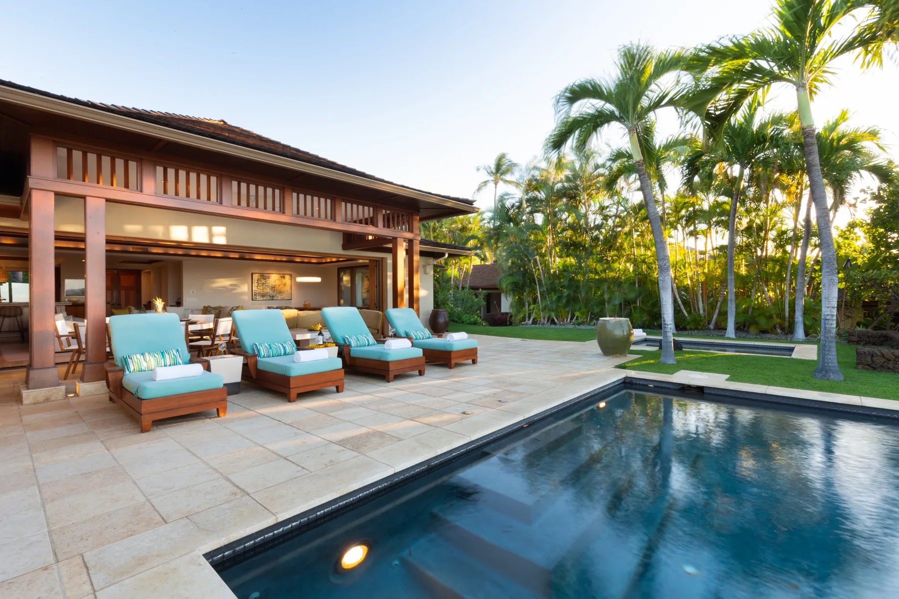 An outdoor pool beside a covered patio with seating and palm trees.