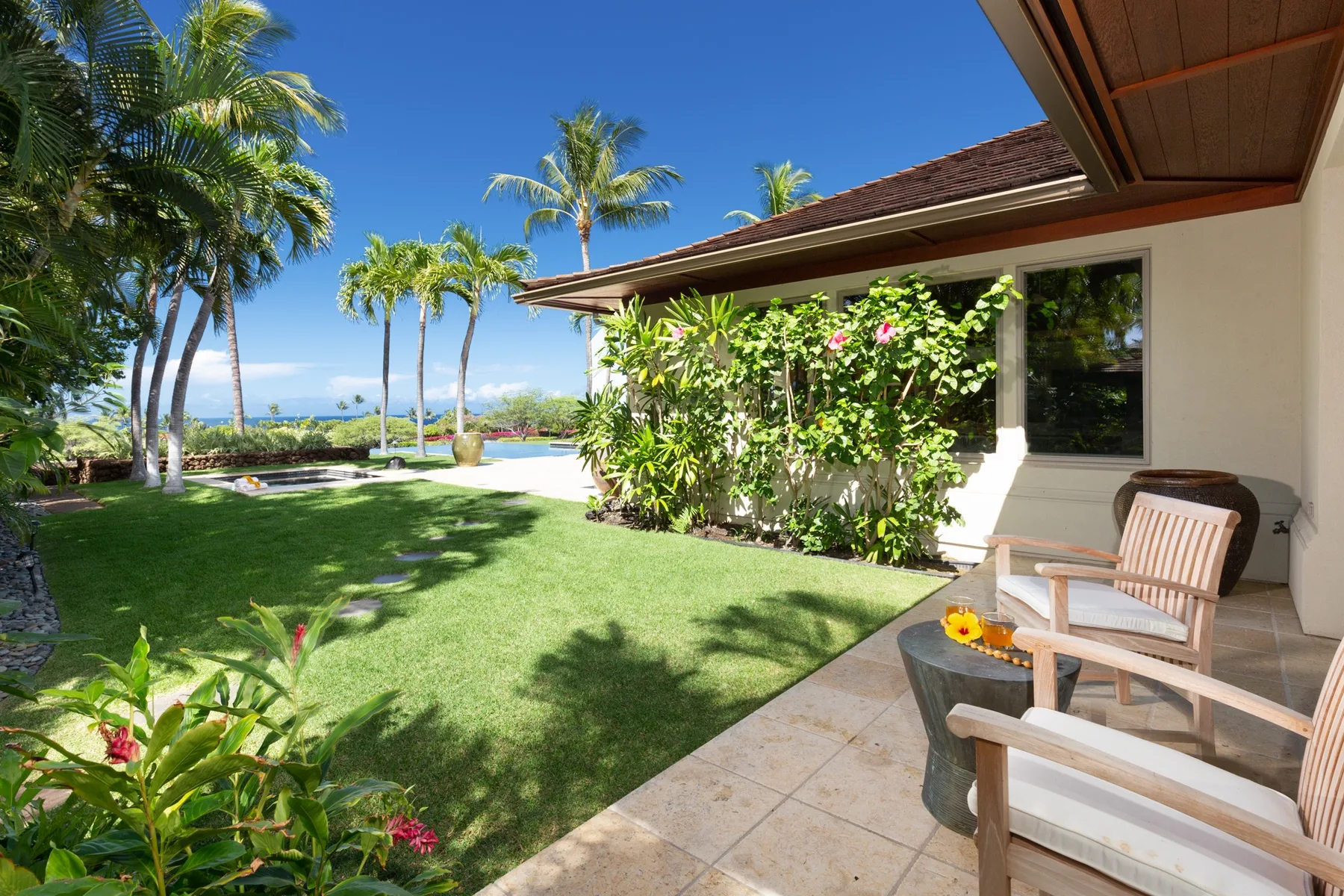 A patio with seating overlooks a green garden and palm trees.