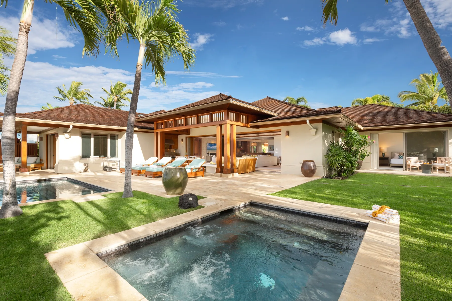 A modern villa opens onto a patio with a swimming pool and palm trees.