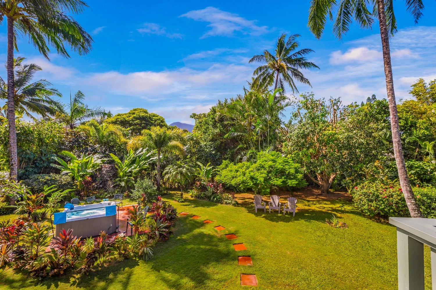 Un jardín tropical tiene césped, piedras para caminar y una pequeña zona para sentarse.