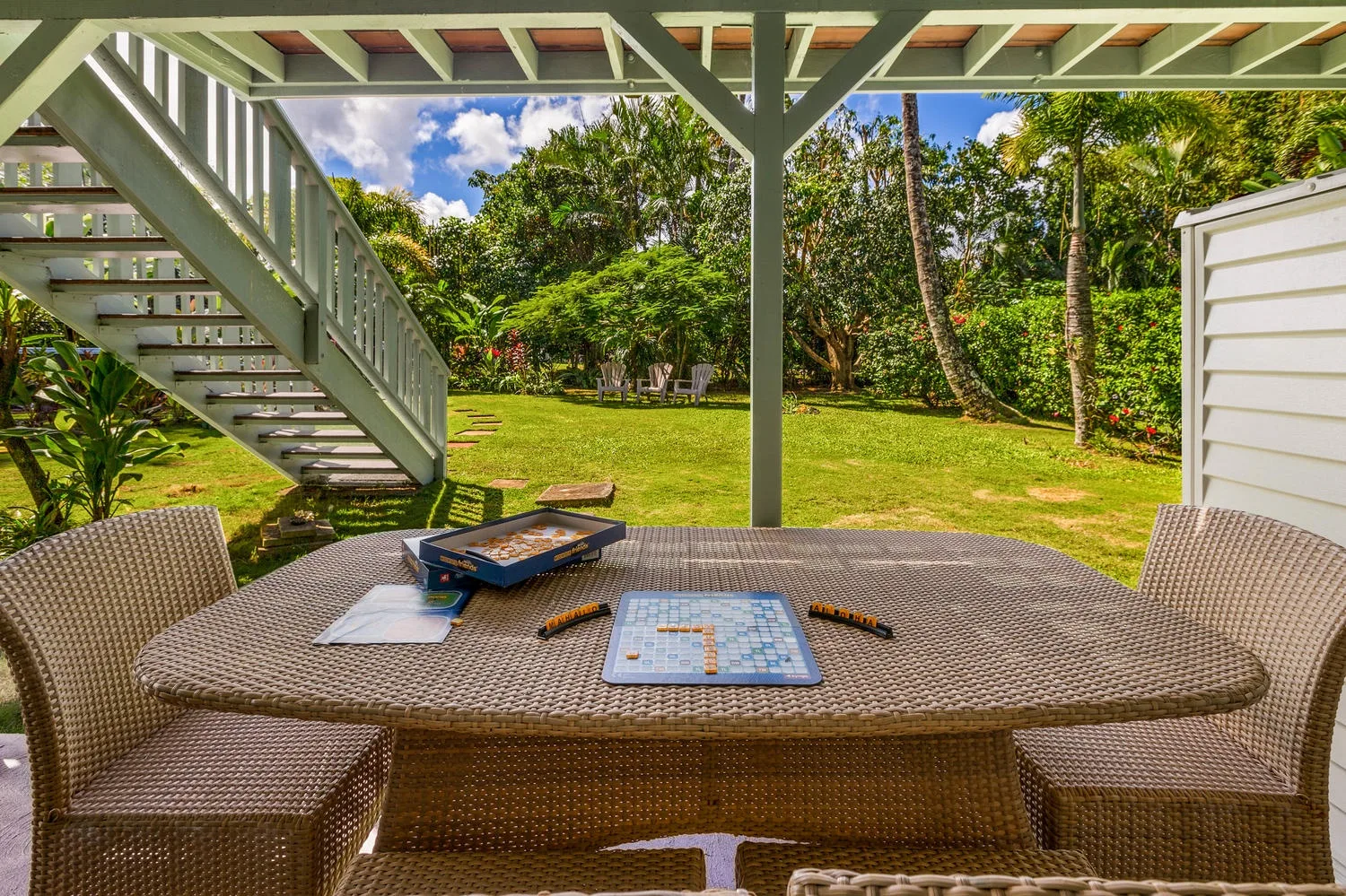 Una mesa de patio está bajo una terraza elevada, frente a un jardín verde.