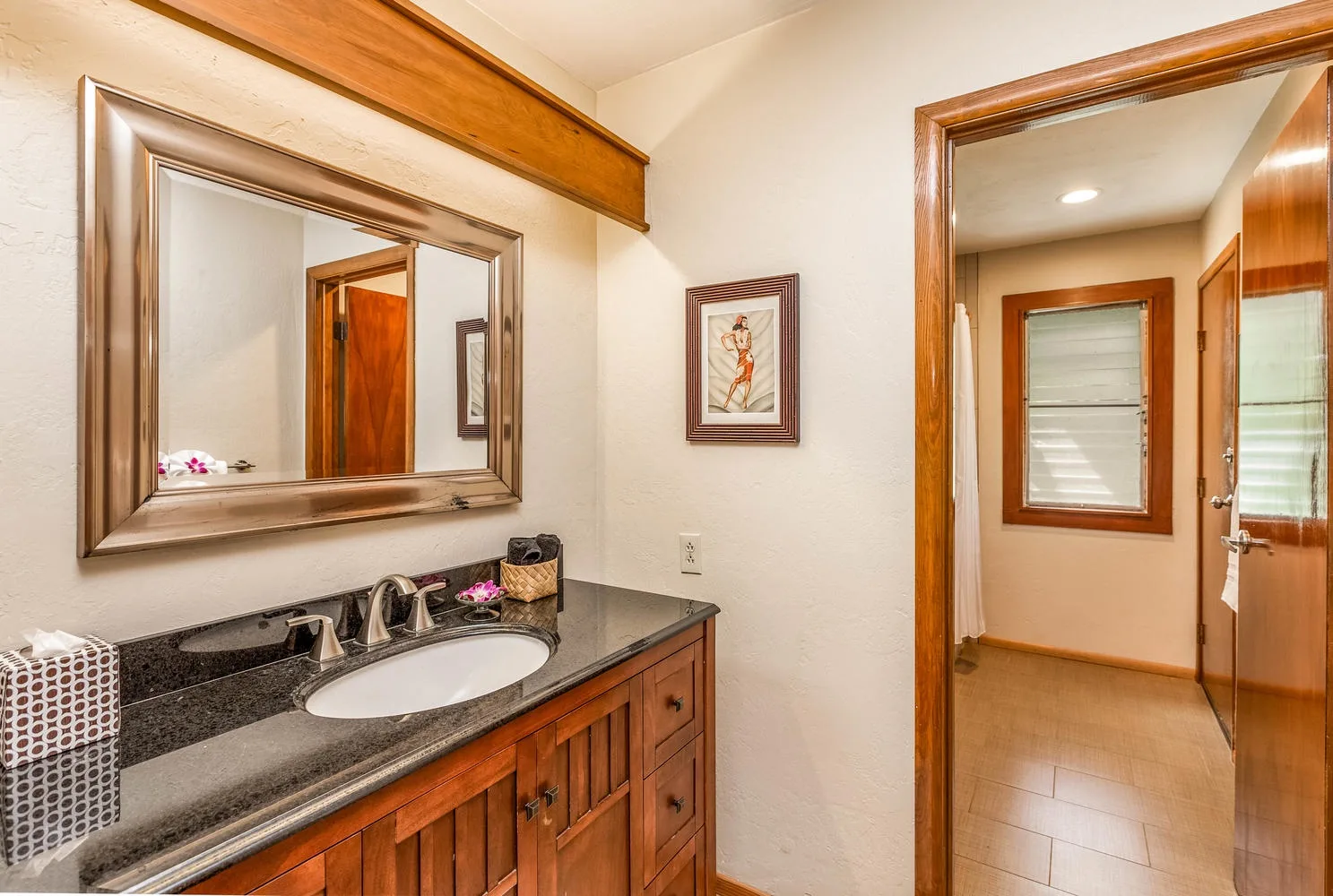 Un lavabo de baño con espejo da a un pasillo con suelo de baldosas.