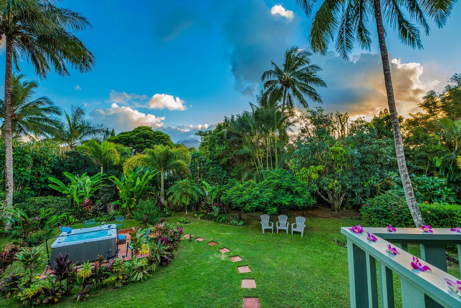 Un jardín tropical con césped, abundante vegetación y una pequeña zona para sentarse.