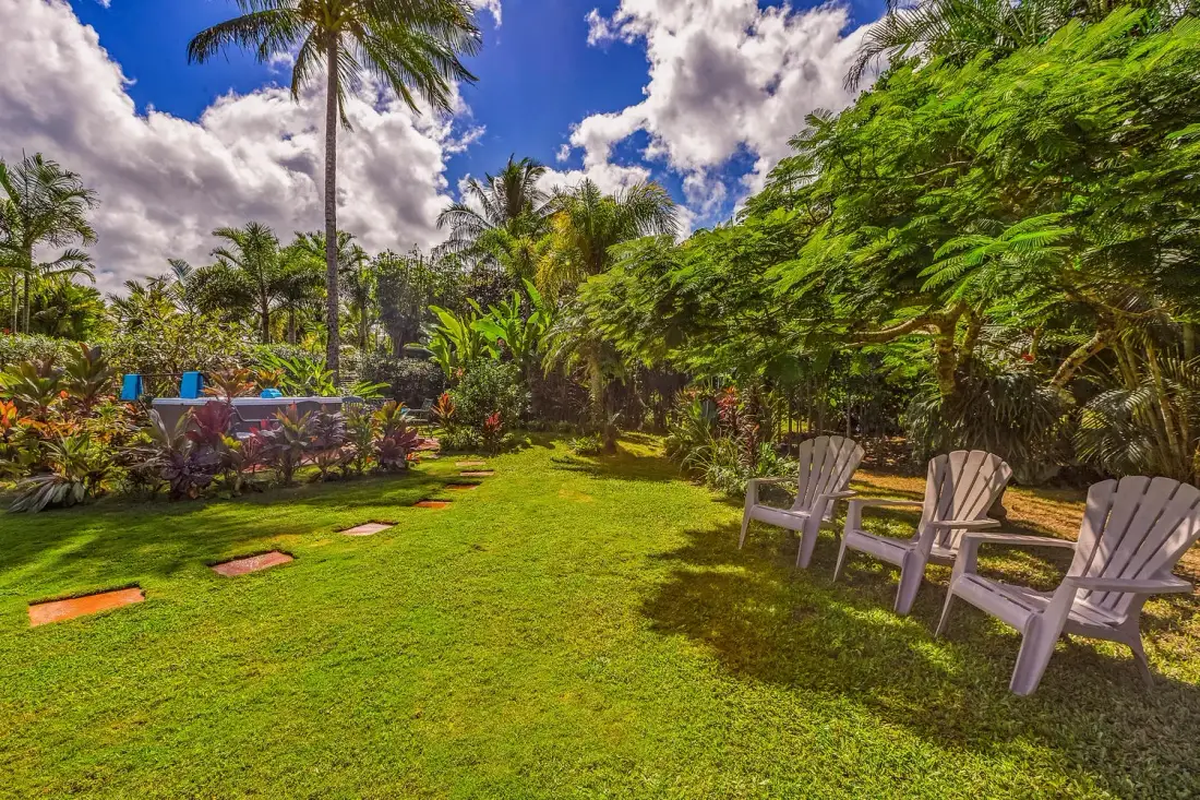 Un jardín tropical con césped, abundante vegetación y asientos al aire libre.