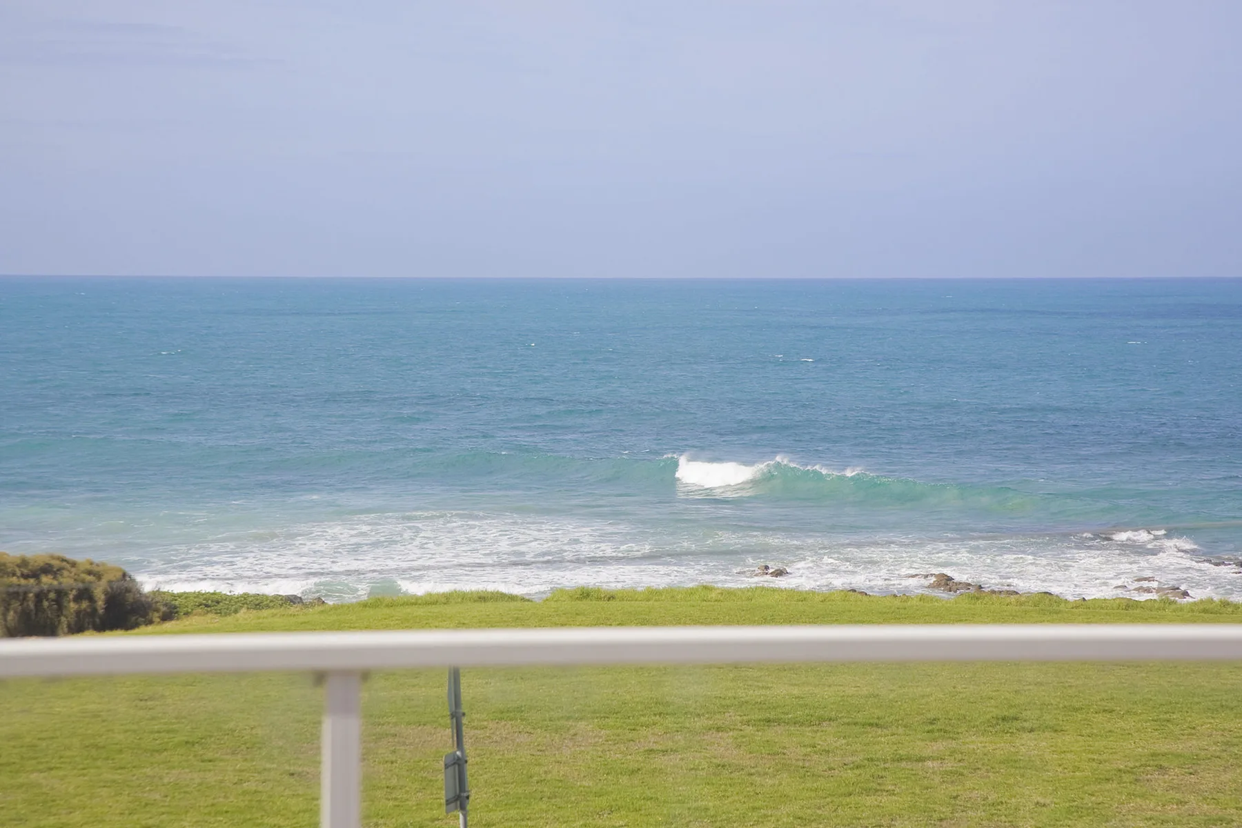 A grassy area borders the ocean, with small waves breaking along the shore.