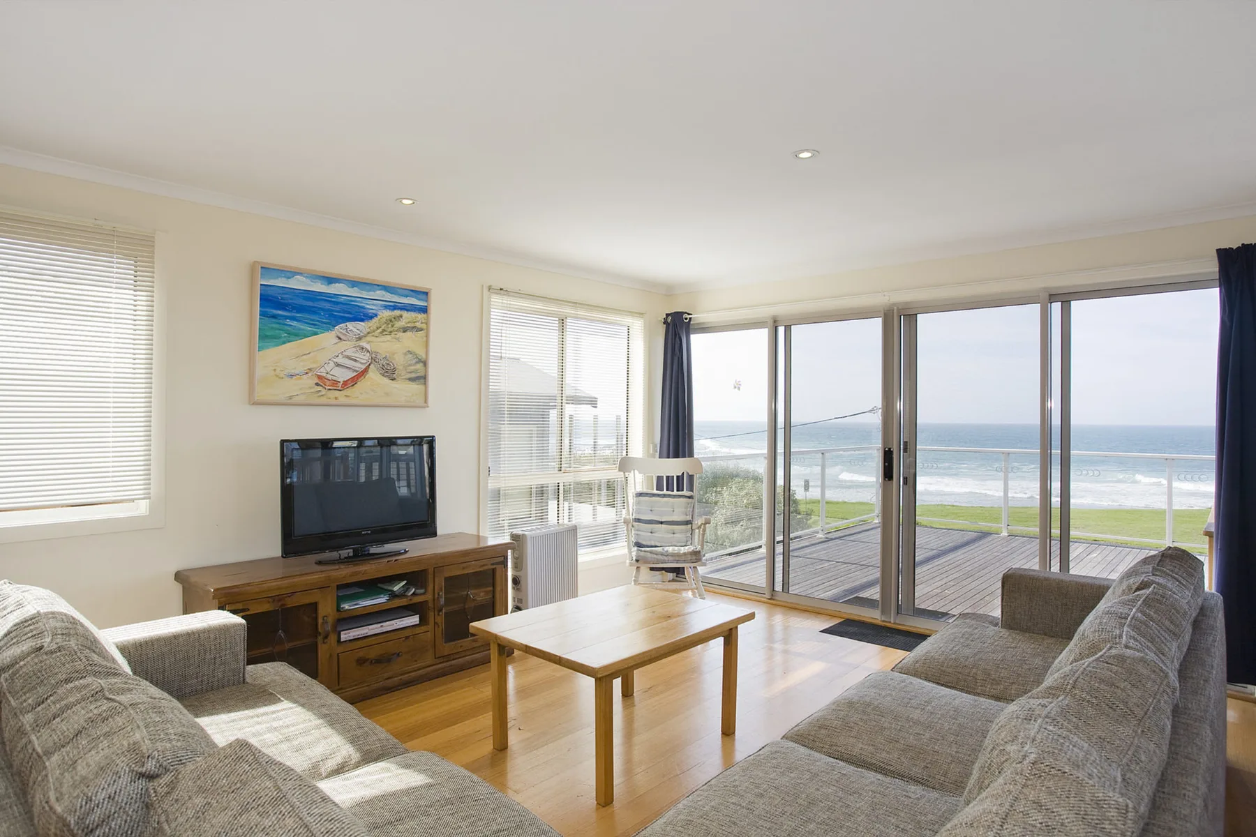 A bright living room opens onto a deck overlooking the ocean.
