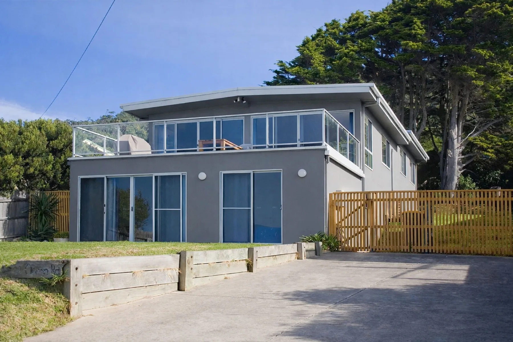A modern gray house with large windows and a paved driveway.