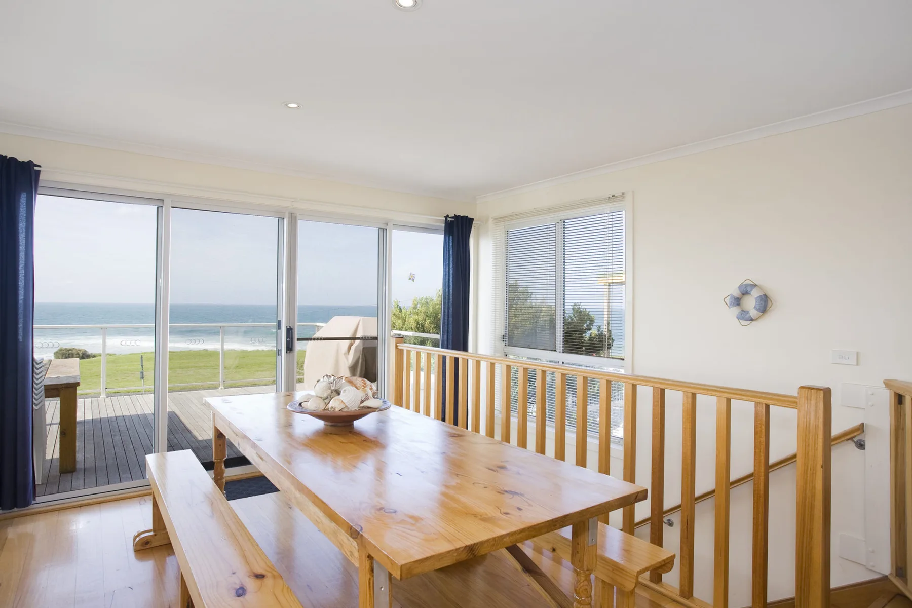 A bright dining area with a wooden table and large windows overlooking the ocean.