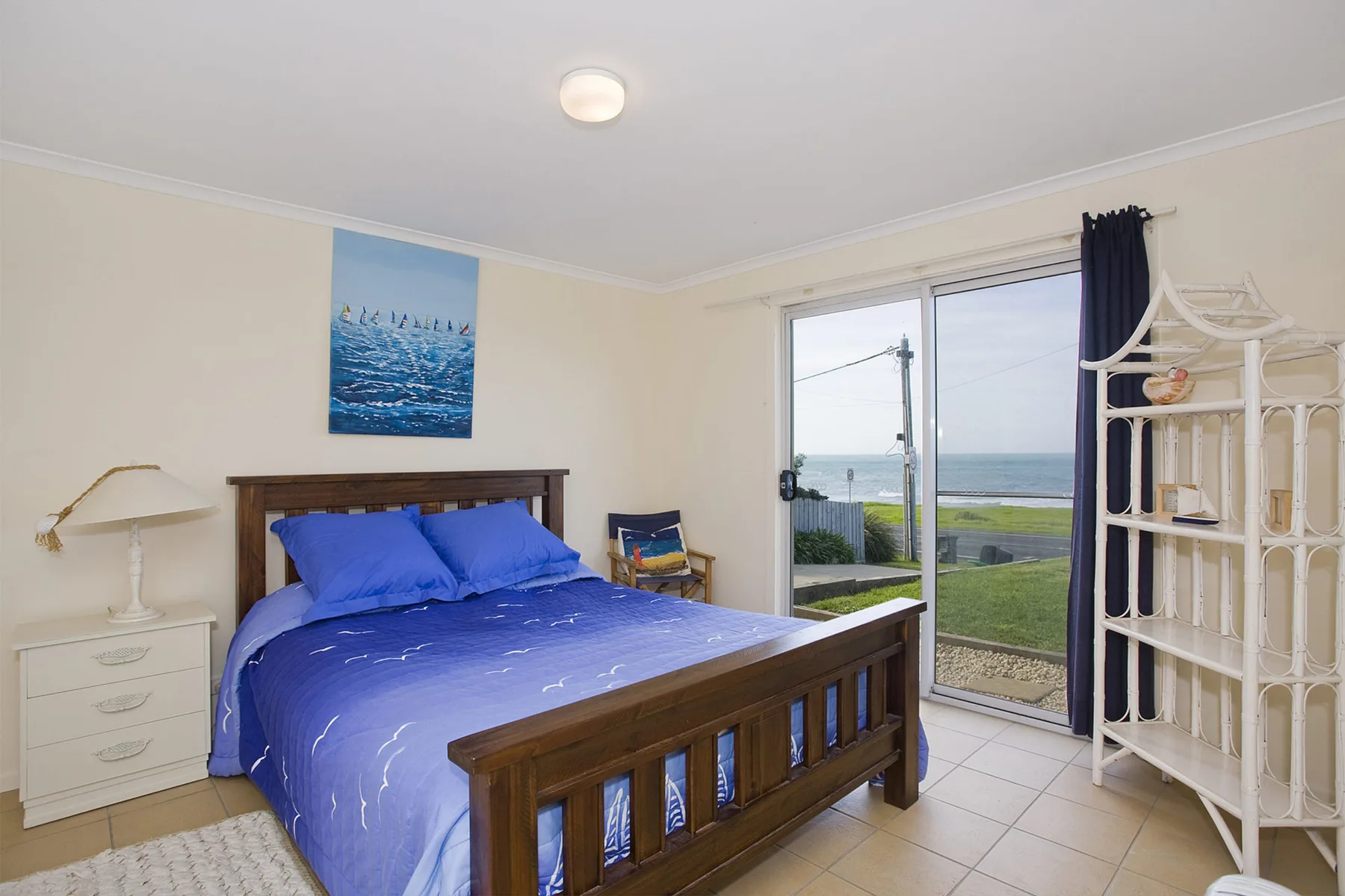 A bedroom with a blue bed beside sliding glass doors overlooking the ocean.
