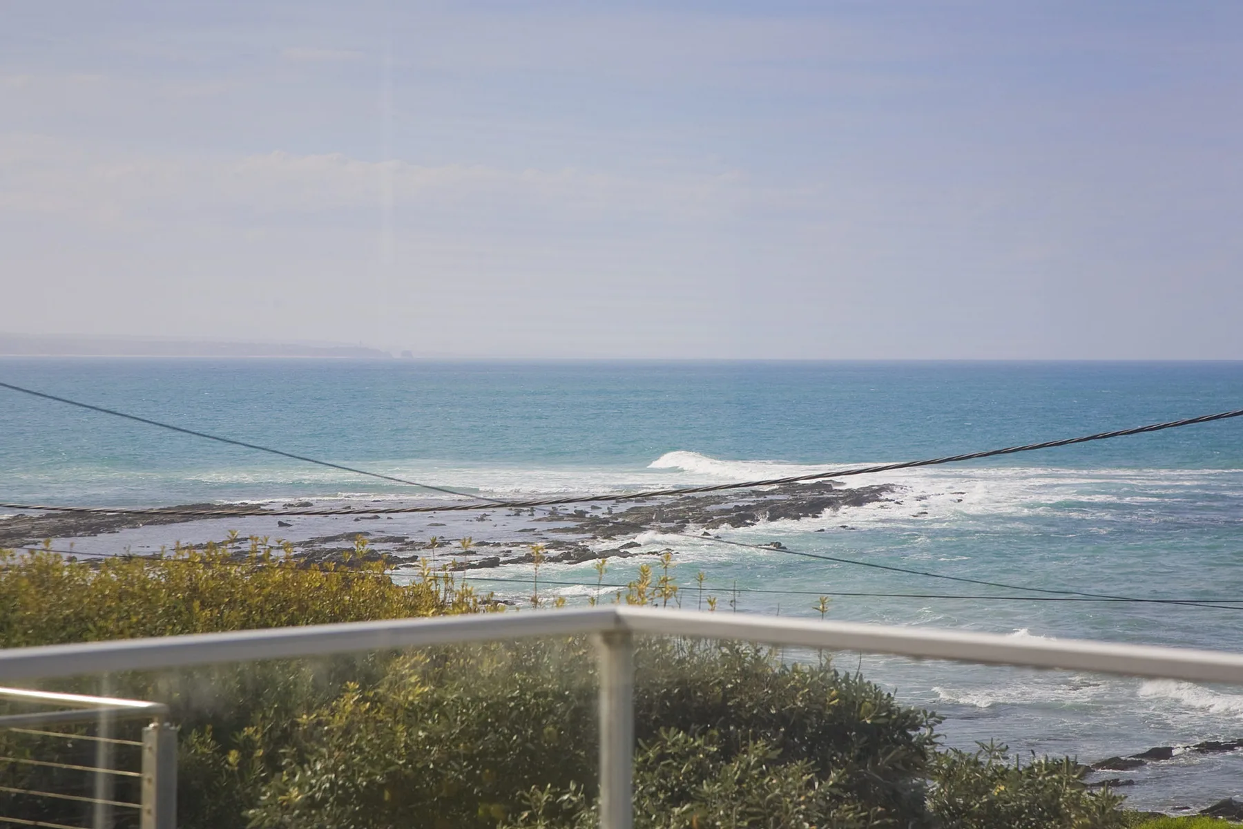 A coastal view with ocean waves and a glass balcony railing.