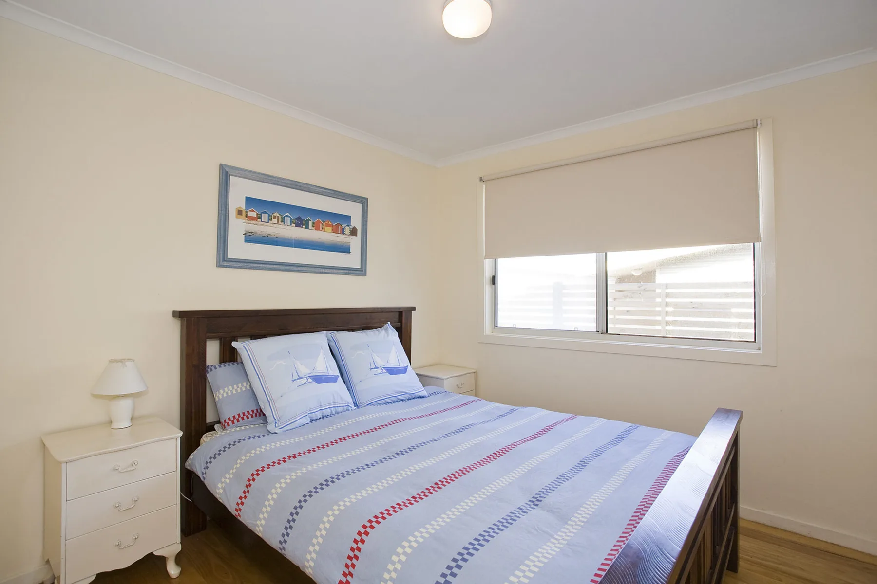 A bedroom with a bed beneath a framed picture and beside a window.