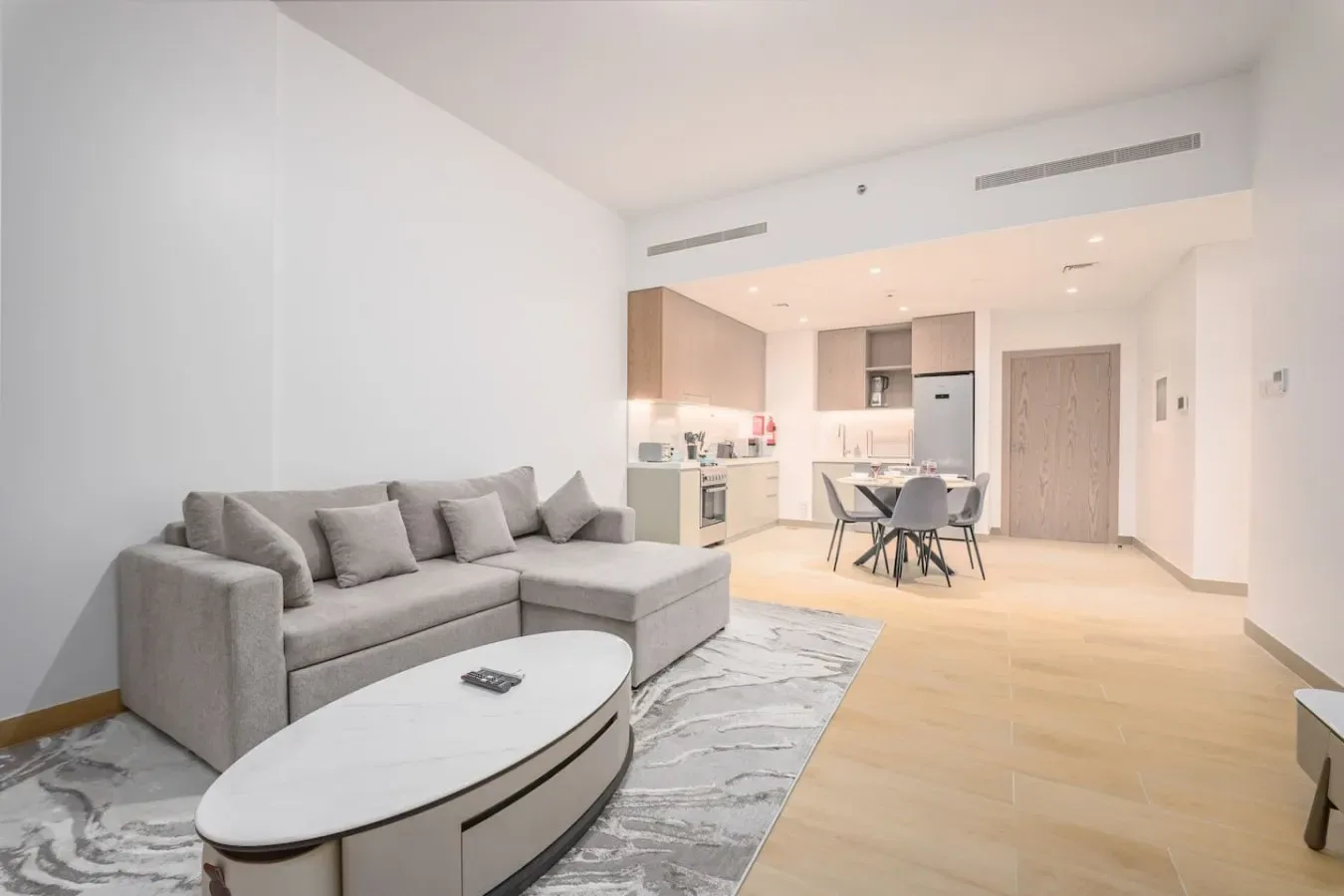 Una luminosa sala-comedor de planta abierta con asientos grises y una cocina al fondo.