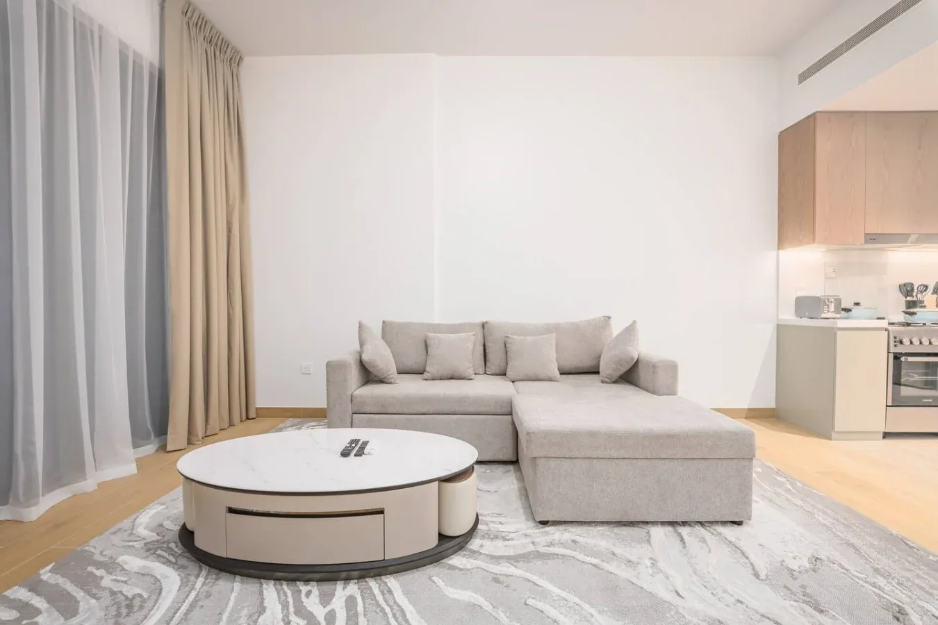 Una sala luminosa con un sofá seccional claro y una mesa de centro redonda.