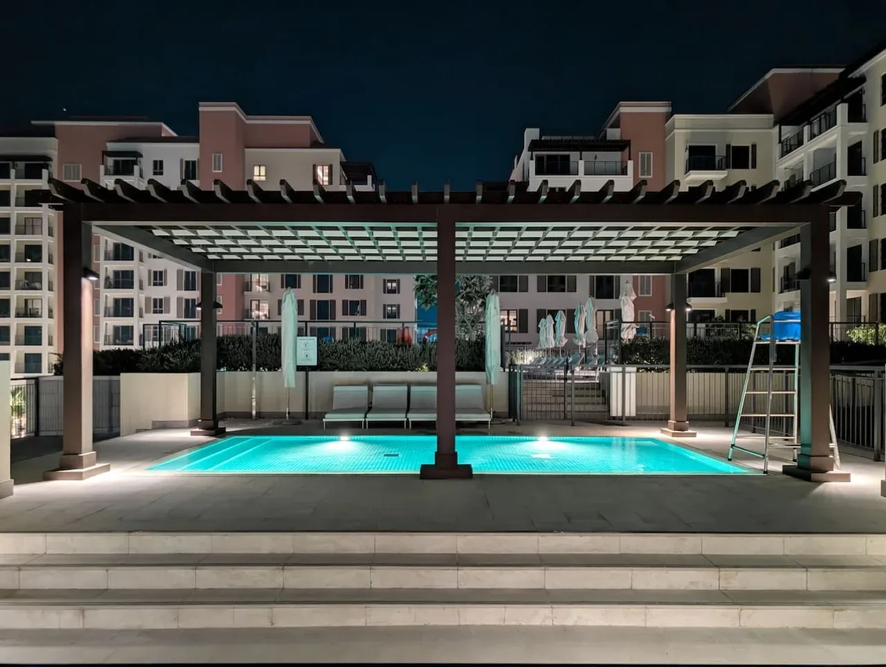 Una piscina exterior iluminada se encuentra bajo una pérgola cubierta por la noche.
