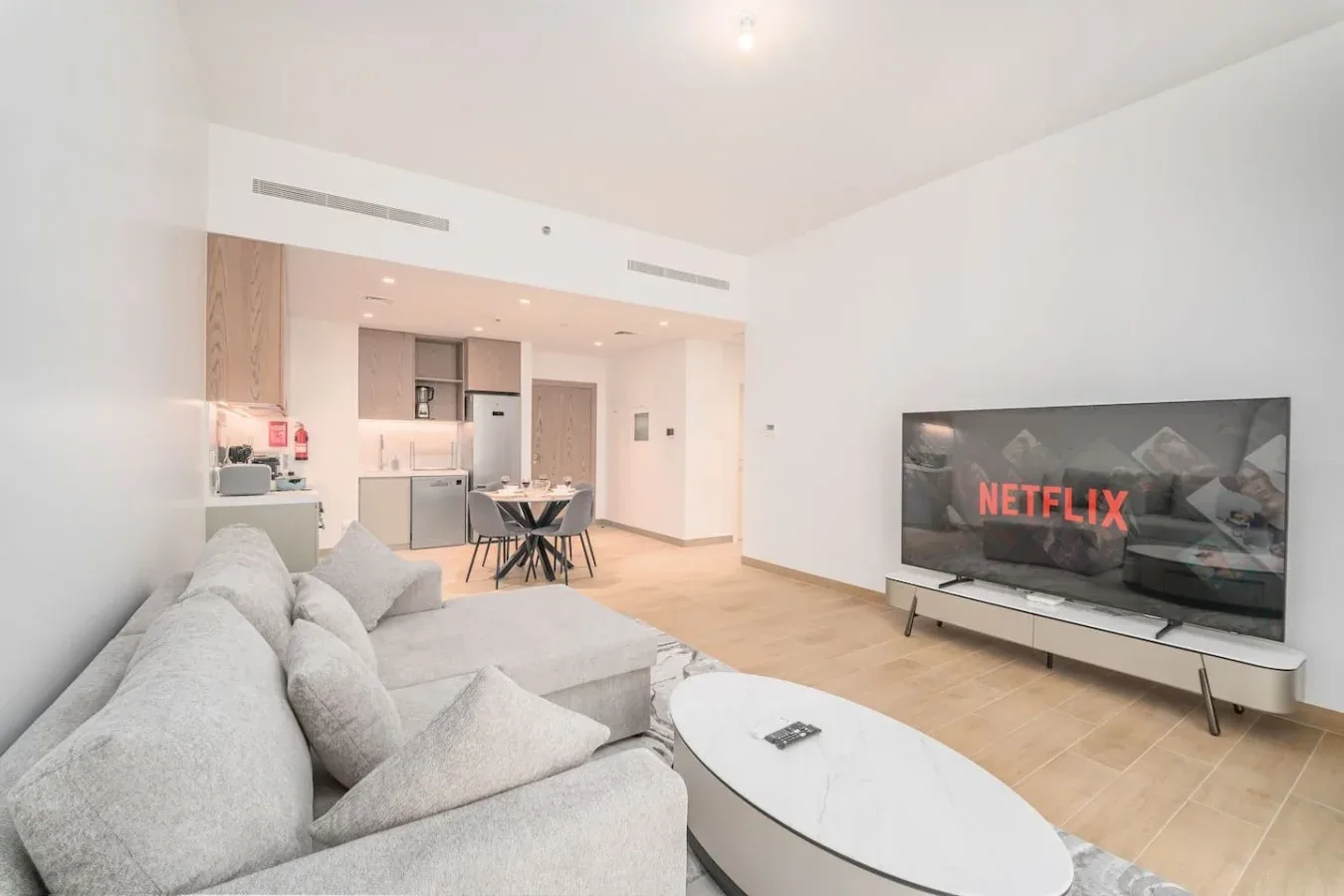 Una luminosa sala de estar de planta abierta con sofá seccional, televisor y cocina.