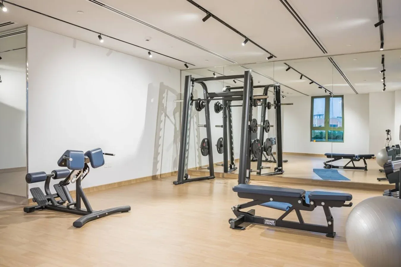 Un gimnasio con máquinas de pesas, bancos de ejercicio y una ventana grande.