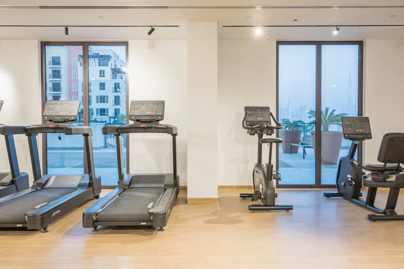 Una sala de ejercicio luminosa con cintas de correr y bicicletas junto a grandes ventanales.
