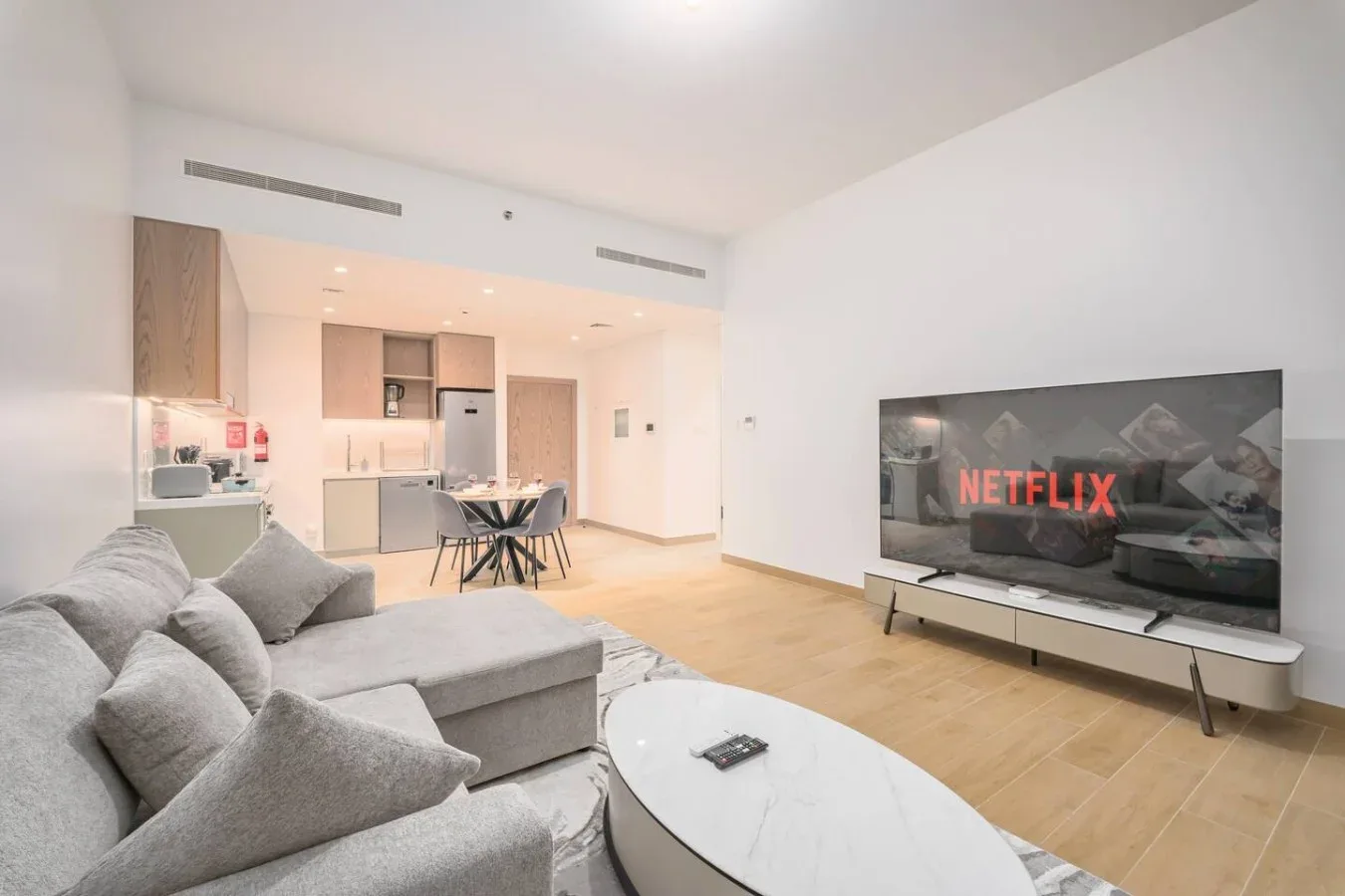 Una sala de estar diáfana con asientos grises, comedor y televisión.