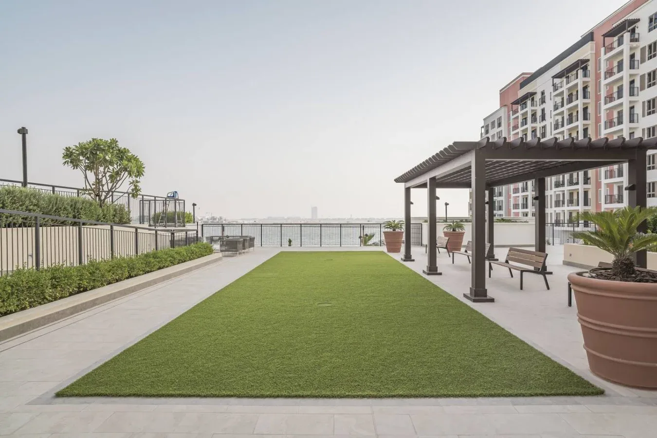 Una terraza en la azotea tiene un amplio césped junto a una pérgola sombreada y asientos.