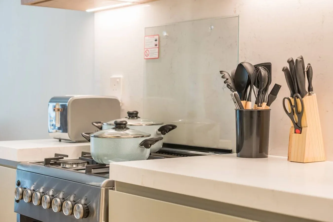 Una cocina con ollas en la estufa, utensilios y una tostadora sobre la encimera.