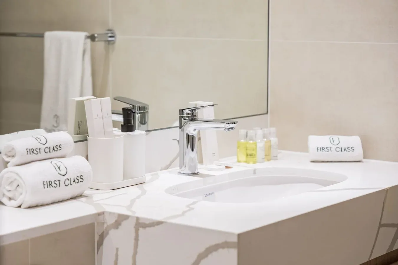 Un tocador de baño con lavabo, espejo, toallas dobladas y artículos de aseo.