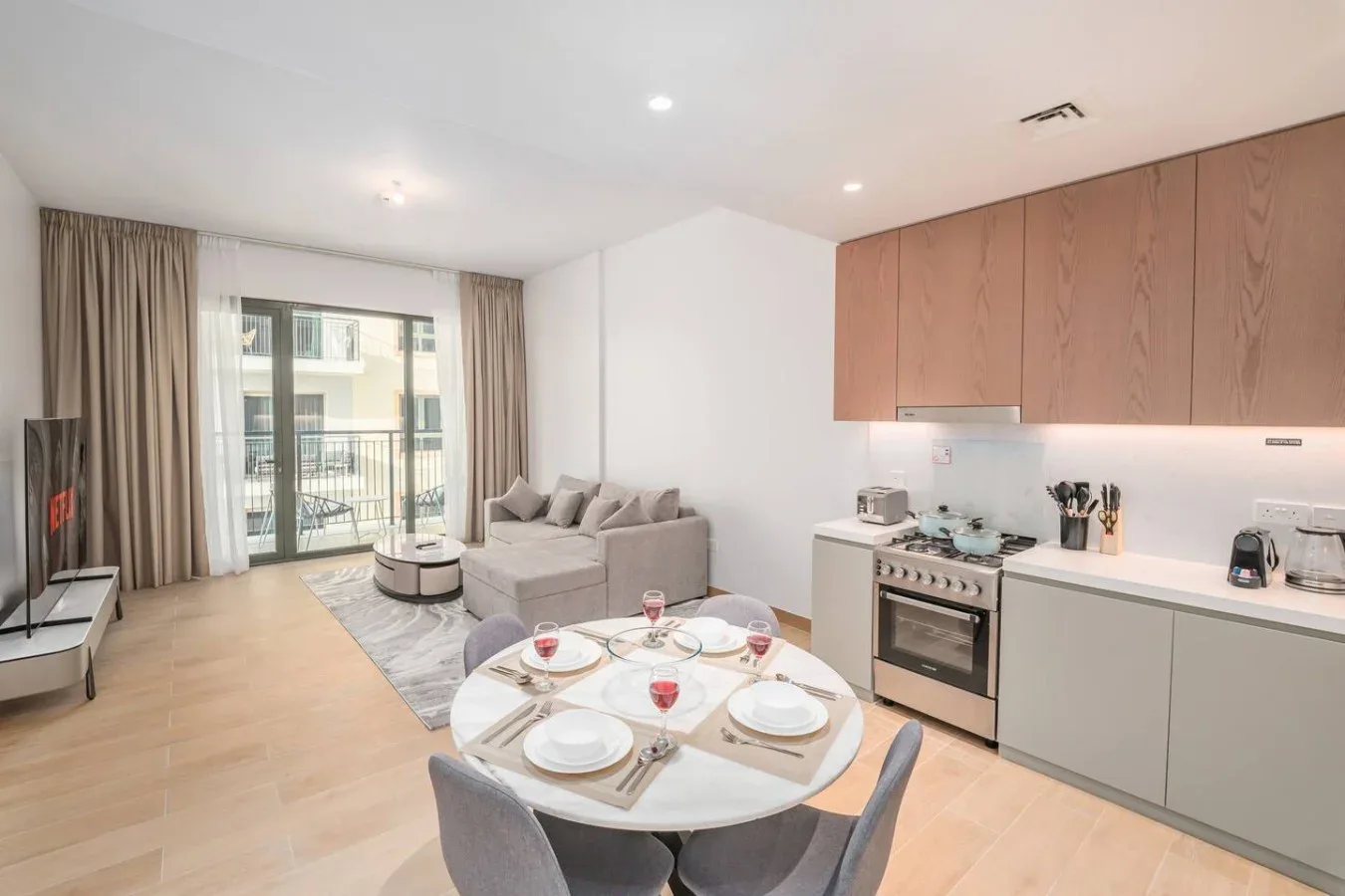 Una luminosa sala de estar con cocina abierta y una mesa de comedor junto a las puertas del balcón.