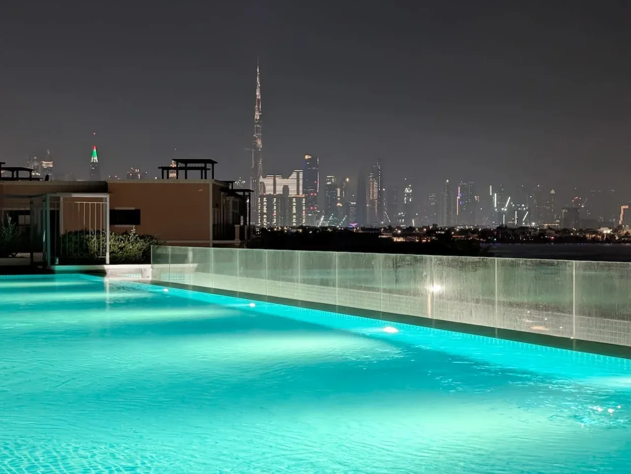 Una piscina en la azotea brilla en tonos turquesa por la noche, con el perfil urbano al fondo.