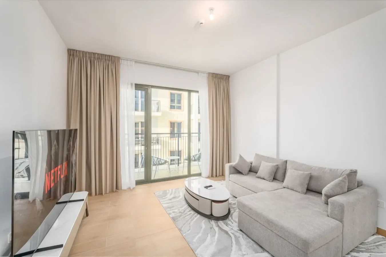 Una sala luminosa con sofá seccional, mesa de centro y puertas de vidrio hacia un balcón.